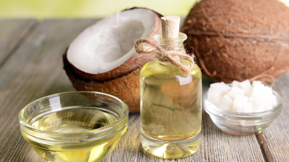 A bottle of body oil sits next to open coconuts and coconut oil - is body oil better than lotion