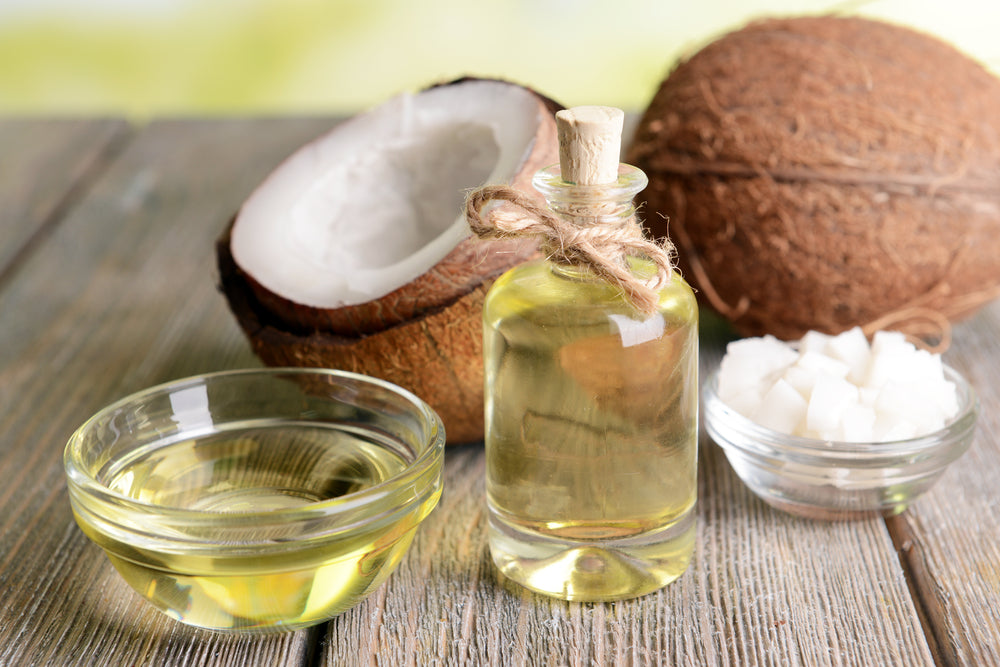 A bottle of body oil sits next to open coconuts and coconut oil - is body oil better than lotion